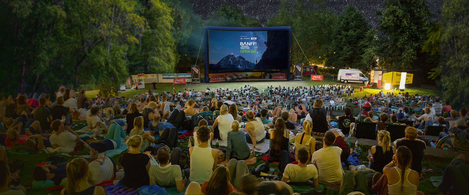 Open-Air-Publikum auf einer Wiese vor einer aufblasbaren Leinwand der Banff Tour bei einer Vorf&uuml;hrung unter freiem Sternenhimmel.